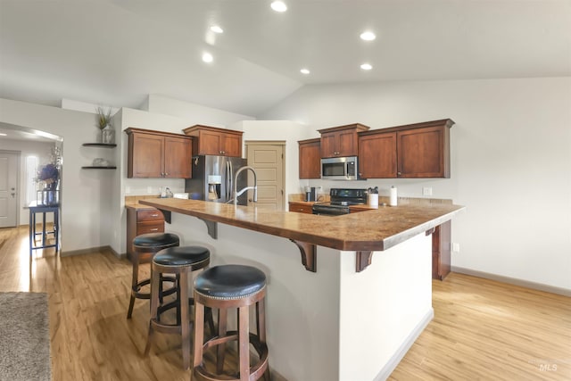 kitchen featuring light wood finished floors, a center island with sink, a kitchen bar, arched walkways, and stainless steel appliances