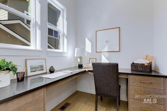 office area featuring visible vents, wood finished floors, and built in desk