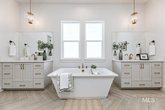 full bathroom with a sink, a freestanding bath, and two vanities