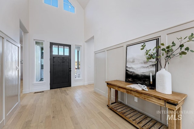 entrance foyer with light wood-style flooring, a decorative wall, a healthy amount of sunlight, and visible vents