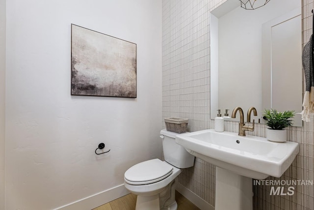 bathroom featuring wood finished floors, baseboards, a sink, tile walls, and toilet