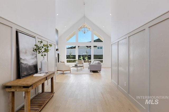 corridor featuring light wood-style flooring, high vaulted ceiling, and a chandelier