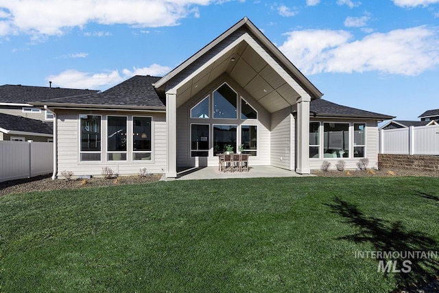 rear view of house with a patio area, a yard, a shingled roof, and fence