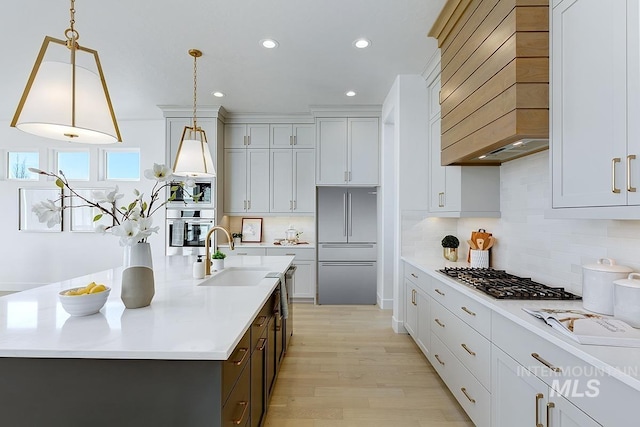 kitchen with light wood-style flooring, custom range hood, a sink, appliances with stainless steel finishes, and light countertops