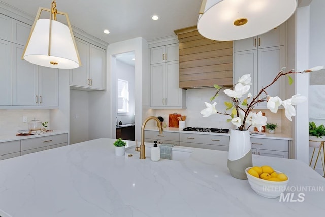 kitchen with decorative light fixtures, decorative backsplash, light stone countertops, and a sink