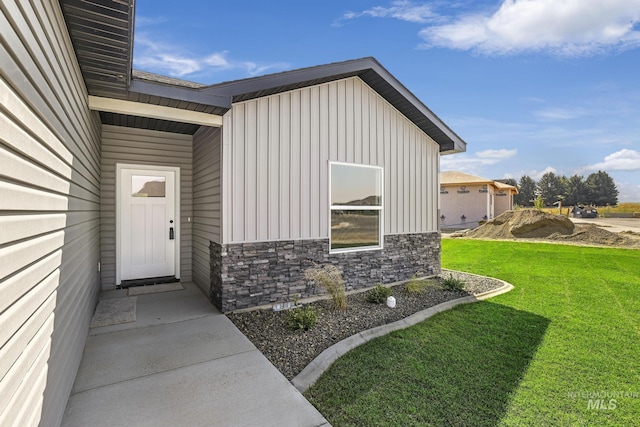 view of exterior entry with stone siding, a lawn, and board and batten siding