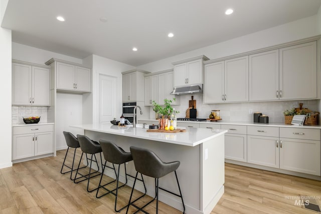 2005 N Spring Creek Ave, Middleton, ID 83644 - kitchen featuring tasteful backsplash, light wood finished floors, under cabinet range hood, a center island with sink, and a kitchen bar