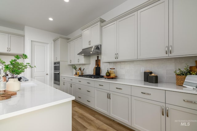 2005 N Spring Creek Ave, Middleton, ID 83644 - kitchen featuring under cabinet range hood, light countertops, light wood-type flooring, tasteful backsplash, and recessed lighting
