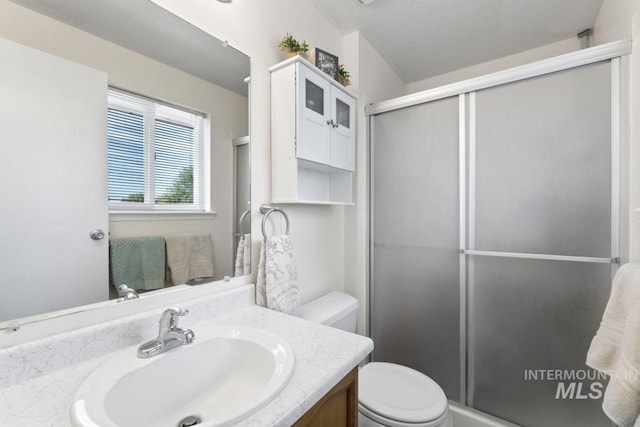 bathroom featuring a shower with door, vanity, and toilet