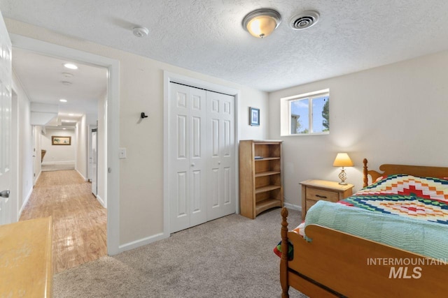 bedroom with light hardwood / wood-style floors, a textured ceiling, and a closet