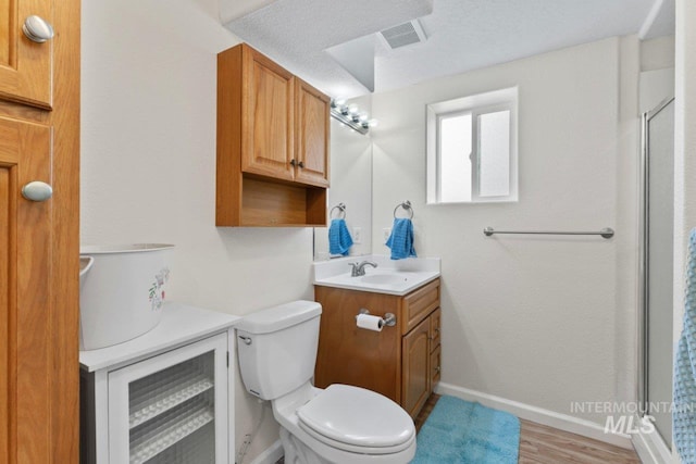 bathroom with a shower with door, toilet, hardwood / wood-style floors, vanity, and a textured ceiling