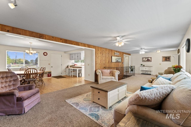 living room with hardwood / wood-style flooring, wooden walls, and ceiling fan with notable chandelier