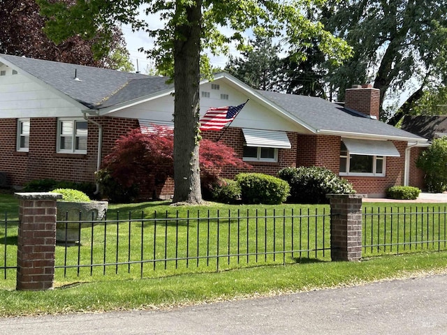 view of front of home with a fenced front yard, brick siding, a chimney, and a front lawn