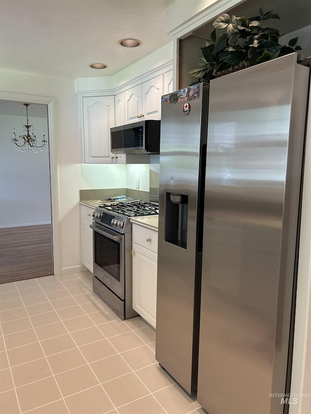 kitchen featuring white cabinets, stainless steel appliances, a chandelier, and light tile patterned floors