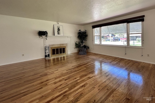 unfurnished living room featuring a textured ceiling, baseboards, wood finished floors, and a premium fireplace