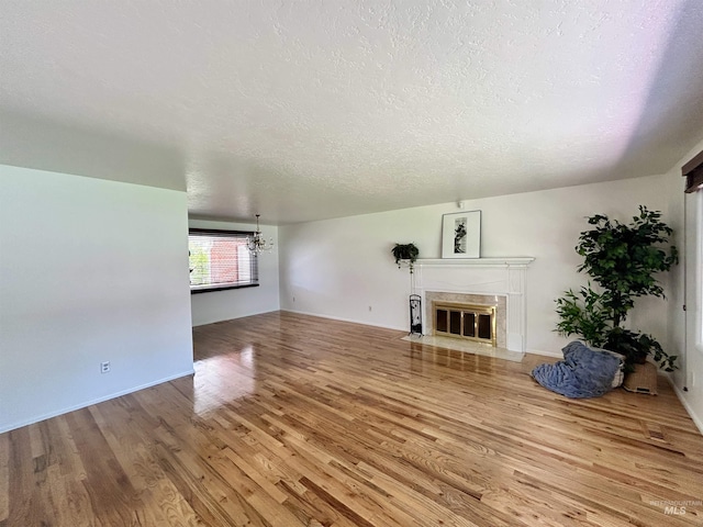 unfurnished living room featuring a premium fireplace, a textured ceiling, a notable chandelier, and wood finished floors