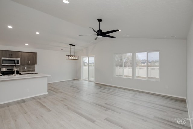 unfurnished living room with sink, ceiling fan with notable chandelier, vaulted ceiling, and light wood-type flooring