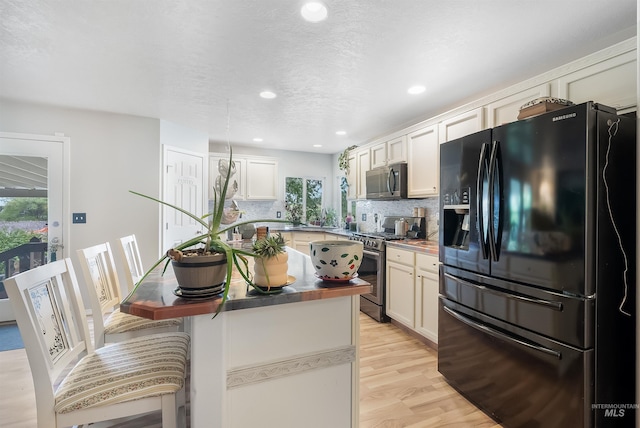 kitchen with plenty of natural light, appliances with stainless steel finishes, light hardwood / wood-style floors, and tasteful backsplash