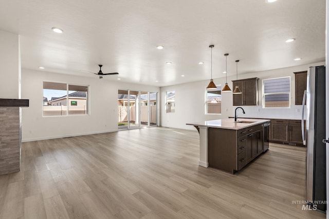 kitchen featuring open floor plan, light countertops, light wood-style flooring, appliances with stainless steel finishes, and a kitchen island with sink