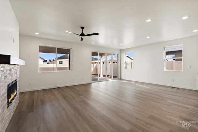 unfurnished living room with a glass covered fireplace, recessed lighting, baseboards, and wood finished floors