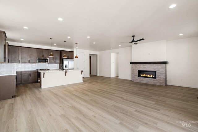 kitchen with stainless steel appliances, dark brown cabinetry, light countertops, a kitchen bar, and backsplash