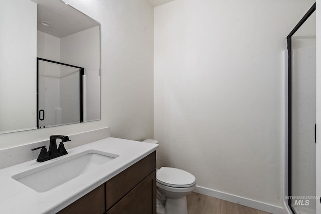 bathroom featuring vanity, wood finished floors, baseboards, a shower stall, and toilet