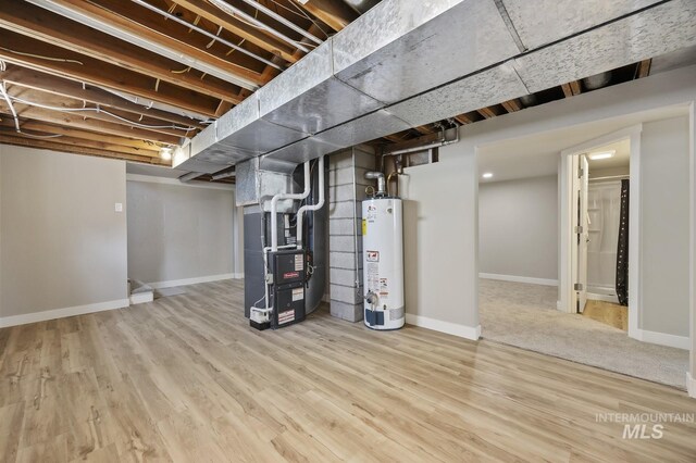 finished below grade area with baseboards, wood finished floors, heating unit, and gas water heater