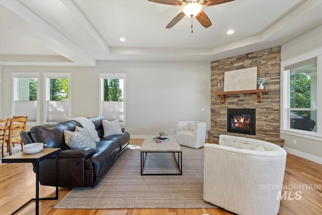 living area with a tray ceiling, ceiling fan, wood finished floors, and a stone fireplace