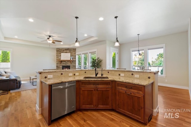 kitchen featuring stainless steel dishwasher, open floor plan, a sink, a tray ceiling, and a stone fireplace