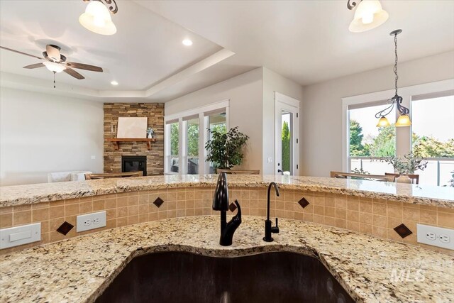 kitchen with a sink, a stone fireplace, decorative backsplash, light stone countertops, and recessed lighting