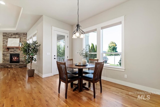 dining room featuring light wood finished floors, baseboards, a stone fireplace, and a chandelier