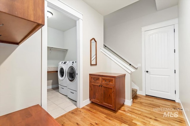 clothes washing area featuring washer and clothes dryer, light wood-style floors, and baseboards