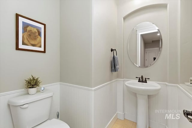 bathroom featuring a wainscoted wall, toilet, tile patterned flooring, and a sink