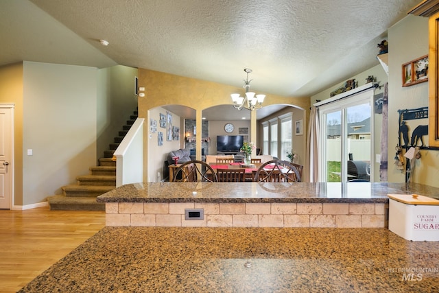 kitchen featuring a textured ceiling, vaulted ceiling, pendant lighting, light hardwood / wood-style flooring, and a chandelier