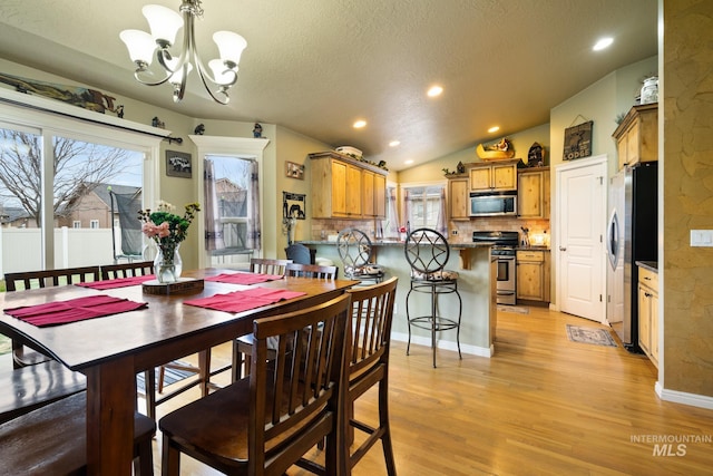 dining room featuring a notable chandelier, a healthy amount of sunlight, light wood-type flooring, and lofted ceiling