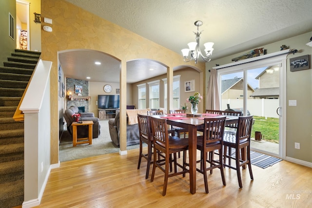 dining space with a notable chandelier, a stone fireplace, light wood-type flooring, and a textured ceiling