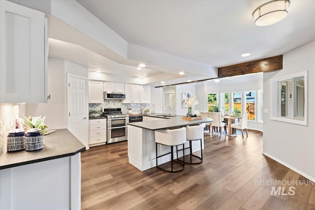 11298 W Charitan St, Boise, ID 83713 - kitchen with appliances with stainless steel finishes, dark countertops, dark wood-style floors, white cabinets, and a breakfast bar area