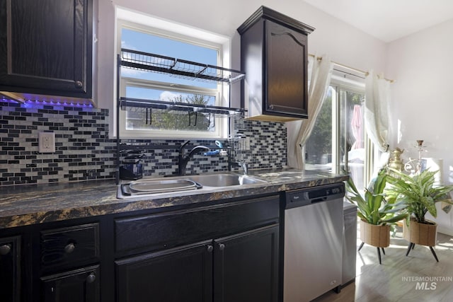 kitchen with dark countertops, decorative backsplash, dishwasher, and a sink