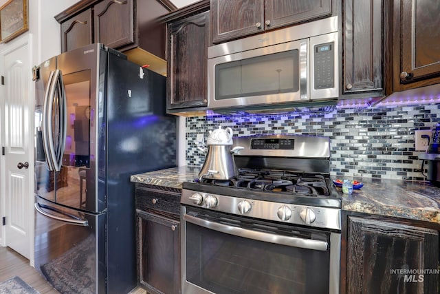 kitchen featuring dark stone countertops, backsplash, stainless steel appliances, light hardwood / wood-style flooring, and dark brown cabinetry