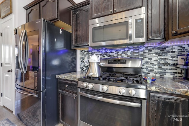kitchen with dark brown cabinetry, backsplash, stainless steel appliances, and dark stone countertops