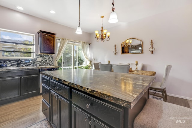 kitchen with light wood-style flooring, a sink, backsplash, dark countertops, and an inviting chandelier