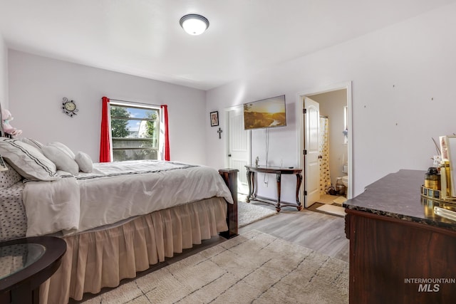 bedroom with connected bathroom and light wood-style floors