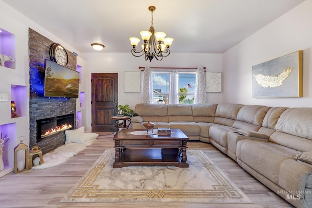 living room with a notable chandelier, a stone fireplace, and wood finished floors