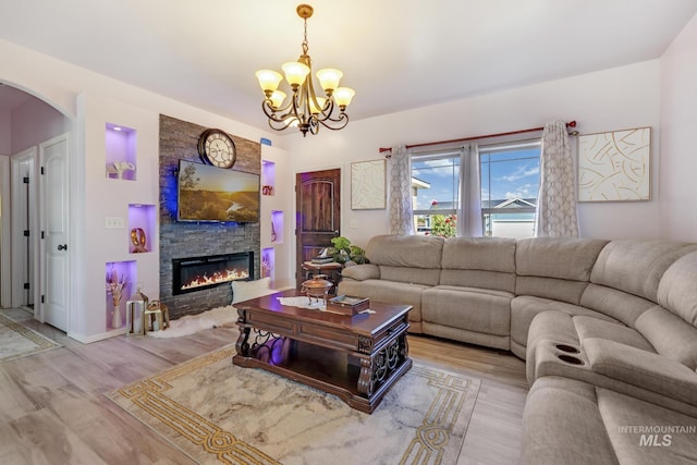 living area with light wood-style floors, arched walkways, a notable chandelier, and a stone fireplace