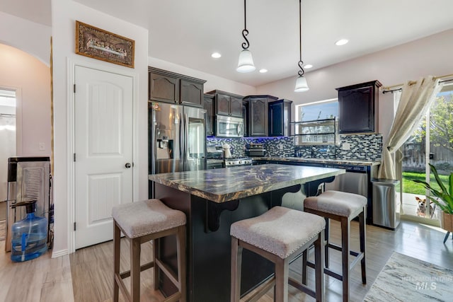 kitchen featuring appliances with stainless steel finishes, backsplash, a center island, light hardwood / wood-style flooring, and decorative light fixtures