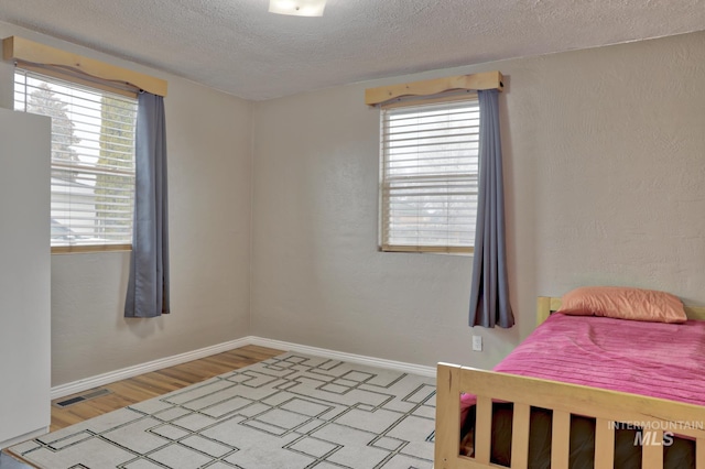 bedroom with multiple windows, light hardwood / wood-style floors, a textured ceiling, and white refrigerator