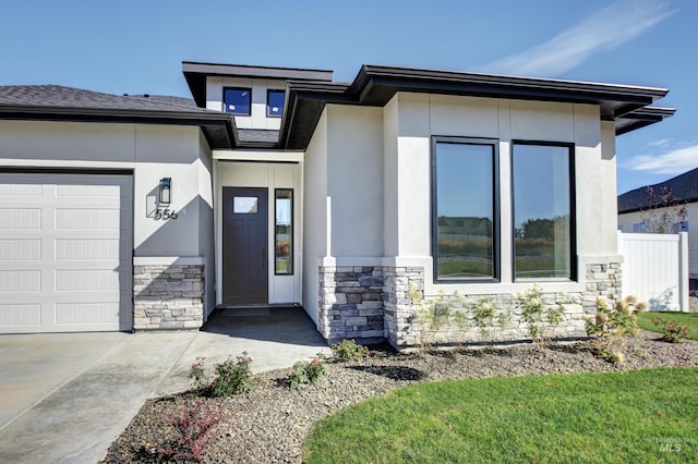 view of exterior entry with an attached garage, stone siding, and stucco siding