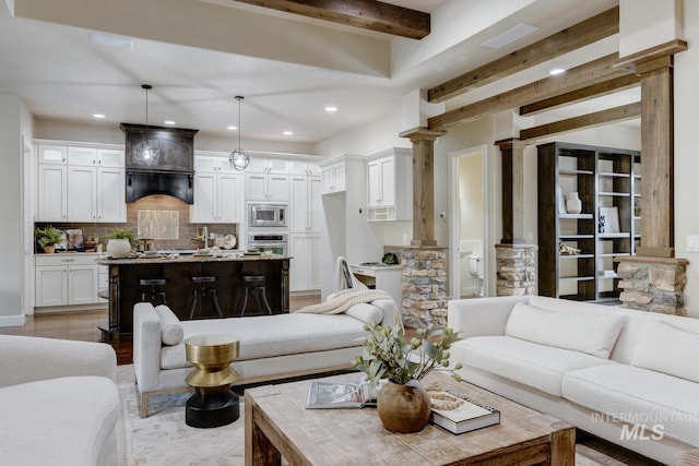 living room featuring beamed ceiling and ornate columns