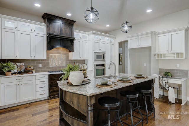 kitchen with white cabinets, hanging light fixtures, and an island with sink