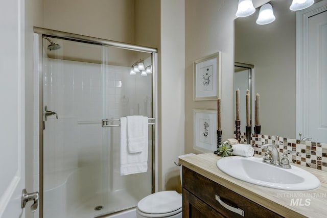 bathroom featuring a shower with shower door, toilet, vanity, and tasteful backsplash